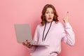 Portrait of surprised curly haired teenage girl with big eyes in hoodie pointing finger up and holding laptop, having an idea Royalty Free Stock Photo