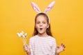 Portrait of surprised cute little girl with rabbit ears with cake pops in hands, looking at camera with amazement, saying wow, Royalty Free Stock Photo