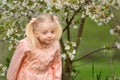 Portrait of surprised or frustrated little girl outside near flowering tree with funny grimace on her face. Spring day