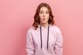 Portrait of surprised funny teen girl with curly hair in hoodie making fish face grimace with pout lips and looking with confused