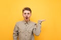 Portrait of surprised geek with glasses and mustache on yellow background, looks surprised at camera and points his hand away at