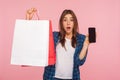 Portrait of surprised girl in checkered shirt holding cellphone and shopping bags, shocked by online store Royalty Free Stock Photo