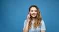 Portrait of a surprised girl with a curly hair dressed in blue t-shirt talking on mobile phone isolated over blue Royalty Free Stock Photo