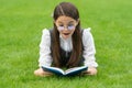 Portrait of surprised girl reading book lying on grass, reading. Teen girl reading outdoors Royalty Free Stock Photo