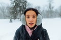 Portrait of surprised hispanic woman in winter clothes outdoors on a snowy day, looking shocked at the camera with open mouth on a Royalty Free Stock Photo