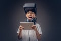 Portrait of a cute little boy dressed in a white t-shirt, with virtual reality glasses and headphones is holding a Royalty Free Stock Photo