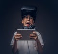 Portrait of a cute little boy dressed in a white t-shirt, with virtual reality glasses and headphones is holding a Royalty Free Stock Photo