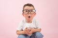 Portrait of a surprised little boy who looks into the camera, in glasses, dressed in white t-shirt, pink background Royalty Free Stock Photo