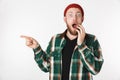 Portrait of surprised man wearing hat and plaid shirt laughing and pointing finger aside, while standing isolated over white Royalty Free Stock Photo