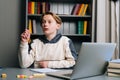 Portrait of surprised pupil boy having idea and raising hand during learning online using laptop at desk, looking away.