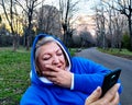 Portrait of surprised senior woman looking at mobile, sitting on bench in park at sunset. Close up Royalty Free Stock Photo