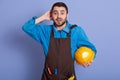 Portrait of surprised shocked construction worker putting hand at back of his head, looking directly at camera with astonishment, Royalty Free Stock Photo