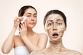 Portrait of a surprised woman with big wrinkles on her face and dry skin, and a beautiful woman doing a gua sha massage Royalty Free Stock Photo