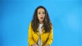 Portrait of surprised woman with curly hair expressing unexpectedness or shock in studio with blue background.