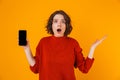 Portrait of surprised woman holding and demonstrating smartphone while standing isolated over yellow background Royalty Free Stock Photo