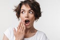 Portrait of surprised woman with short brown hair in basic t-shirt covering her mouth with hand Royalty Free Stock Photo