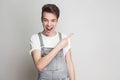 Portrait of surprised young brunette man in casual style with t-shirt and denim overalls standing and looking at camera and point