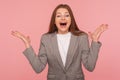 Portrait of surprised young brunette woman in business suit keeping hands raised and shouting in amazement Royalty Free Stock Photo