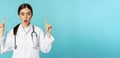 Portrait of surprised young doctor, female medical worker pointing fingers up, gasping amazed, showing health