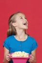 Portrait of surprised young girl holding popcorn container against red background Royalty Free Stock Photo