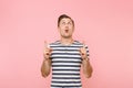 Portrait surprised young man in striped t-shirt pointing index fingers up on copy space, looking up isolated on trending Royalty Free Stock Photo