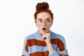 Portrait of surprised young woman student with red hair combed in hairbun, wearing glasses, gasping amazed, look with Royalty Free Stock Photo