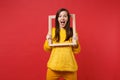 Portrait of surprised young woman in yellow fur sweater keeping mouth wide open holding picture frame isolated on bright