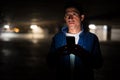 Suspicious-looking Hispanic man thinking while using phone in dark parking lot Royalty Free Stock Photo