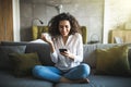 Portrait of a suspicious woman holding phone looking at you sitting on a sofa in the living room of a house Royalty Free Stock Photo