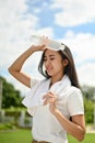 A sweaty Asian woman feeling hot and tired, rests after a long run at the park on a sunny day