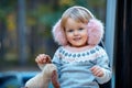 Portrait of sweet blond little baby girl in beautiful warm dress and winter faux fur ear muffs at playground Royalty Free Stock Photo