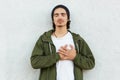 Portrait of sweet handsome youngster leaning on white wall with closed eyes, trying to feel heartbeat with two hands crossed on