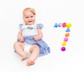 Portrait of a sweet infant baby girl wearing a pink dress and headband bow, isolated on white in studio with number