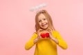 Portrait of sweet lovely angelic little girl with halo over head holding toy hearts and looking at camera