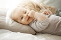 Portrait of sweet smiling newborn daughter lying on cozy bed. Child looks at camera and touching face with her little