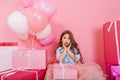 Portrait sweet surprised birthday kid looking to camera suround a lot of giftboxes, balloons on pink background