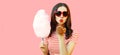 Portrait of sweet young woman blowing her lips sending air kiss with cotton candy wearing red heart shaped sunglasses on pink Royalty Free Stock Photo