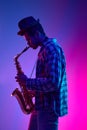Portrait of talented solo saxophonist playing piece against pink-blue gradient background in neon light. Ad