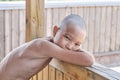 Portrait of tanned asian boy with naked torso, hair cut bald, looking at camera