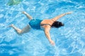 Portrait of tanned middle-aged woman wearing blue swimsuit, floating on stomach in swimming pool, relaxing on sunny day. Royalty Free Stock Photo