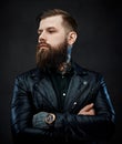 Tattooed cool bearded man in a leather jacket in a dark studio