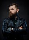 Tattooed cool bearded man in a leather jacket in a dark studio