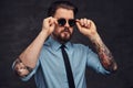 Portrait of a tattooed handsome middle-aged man with beard and hairstyle dressed in a blue shirt and tie, pose with hand Royalty Free Stock Photo