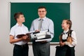 Portrait of a teacher dressed in business suit with folders, documents and briefcase, posing with schoolboy and schoolgirl at