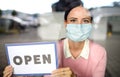 Portrait of teacher with face mask after lockdown, holding open sign.