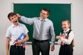 Portrait of a teacher grabs schoolboy`s ear, who has bad discipline, and happy schoolgirl. Posing with exercise books, pens, Royalty Free Stock Photo