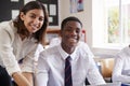 Portrait Of Teacher Helping Pupil Using Computer In Classroom