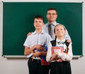 Portrait of a teacher, schoolboy and schoolgirl posing with exercise books, pens, pencils and other school supplies on blackboard Royalty Free Stock Photo