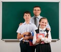 Portrait of a teacher, schoolboy and schoolgirl posing with exercise books, pens, pencils and other school supplies on blackboard Royalty Free Stock Photo