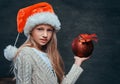 Teen boy wearing Santa`s hat holding a big Christmas ball on a dark textured background. Royalty Free Stock Photo